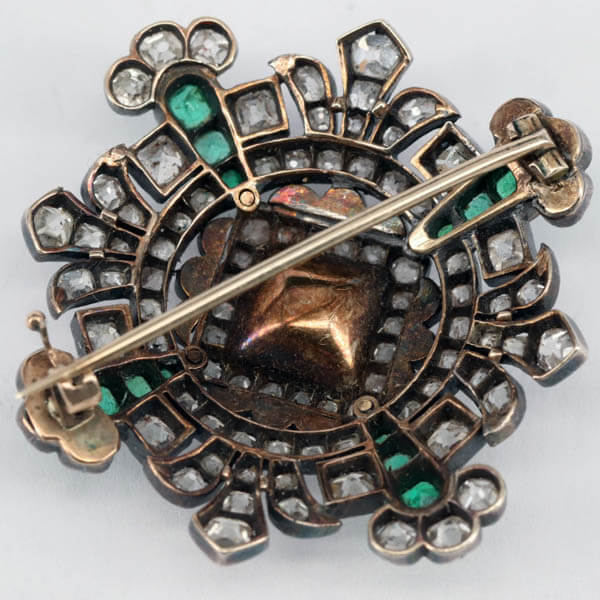 The back side of an antique diamond and emerald brooch which shows discoloration of the metal in order to illustrated oxidation