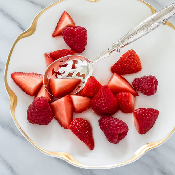 A close-up of a silver berry spoon and a spoonful of berries on a white limoges gold rimmed plate